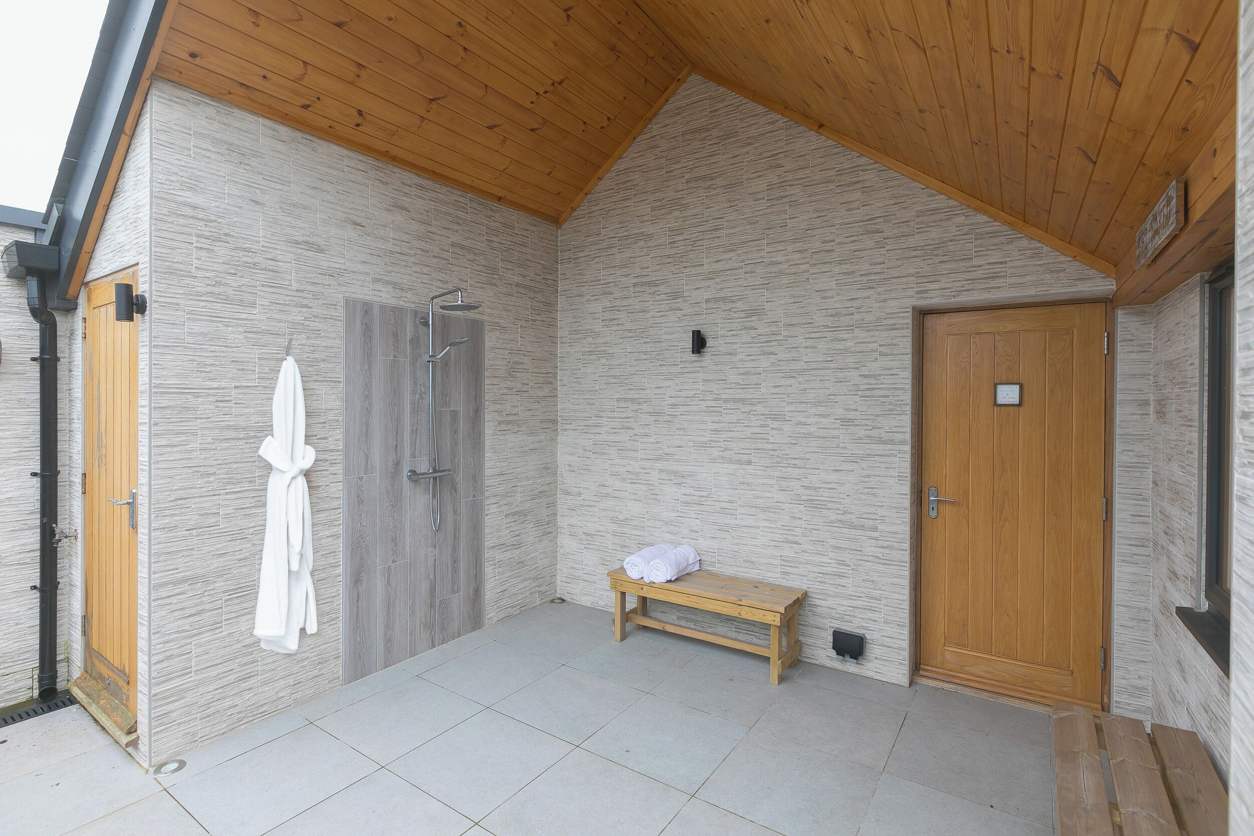 Un espacio de spa con un banco de madera, un perchero y una puerta de madera.