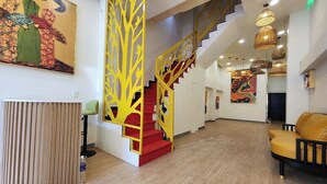A modern interior with a wooden floor, a staircase with red steps and yellow railings, a yellow sofa, and artwork on the walls. - SOHO Suites - BenThanh Market & SG Heart (Ho Chi Minh City)