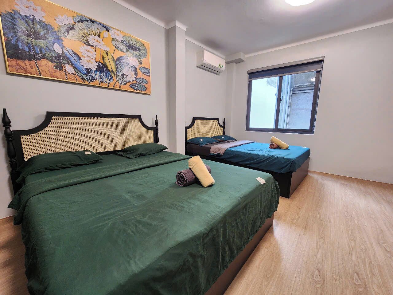 A room with two beds, a window, and a painting on the wall.