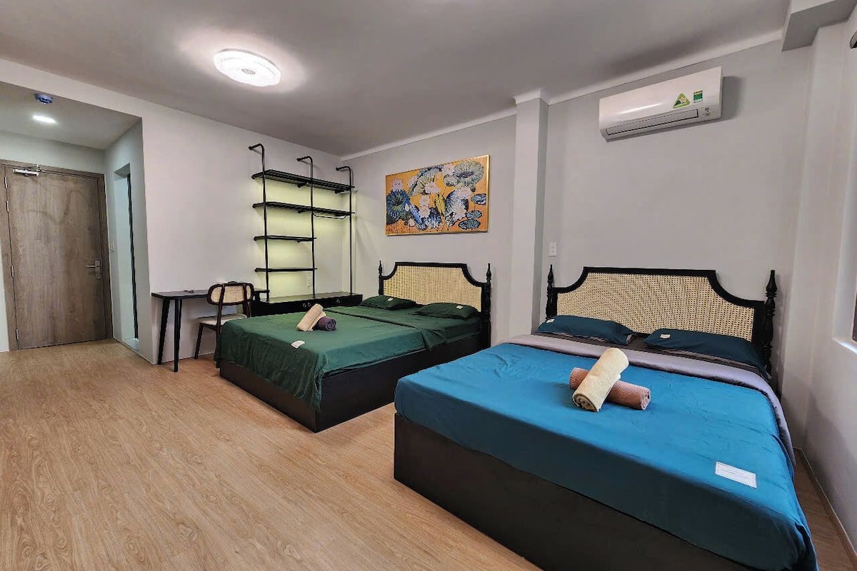 Ein Zimmer mit zwei Betten, einem Schreibtisch und einem Stuhl. An der Wand hängt ein Gemälde und es gibt eine Klimaanlage.