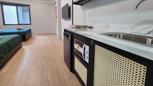 A compact kitchen with a sink, a dishwasher, and a microwave. There is a small seating area with a sofa and a TV mounted on the wall. - SOHO Suites - BenThanh Market & SG Heart (Ho Chi Minh City)