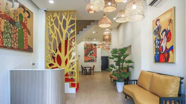 A reception area with a modern desk, a yellow decorative partition, and a sofa. - SOHO Suites - BenThanh Market & SG Heart (Ho Chi Minh City)