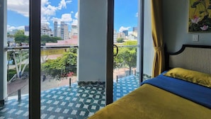 A hotel room with a large window, a bed with blue and yellow bedding, and a view of the cityscape. - SOHO Suites - BenThanh Market & SG Heart (Ho Chi Minh City)