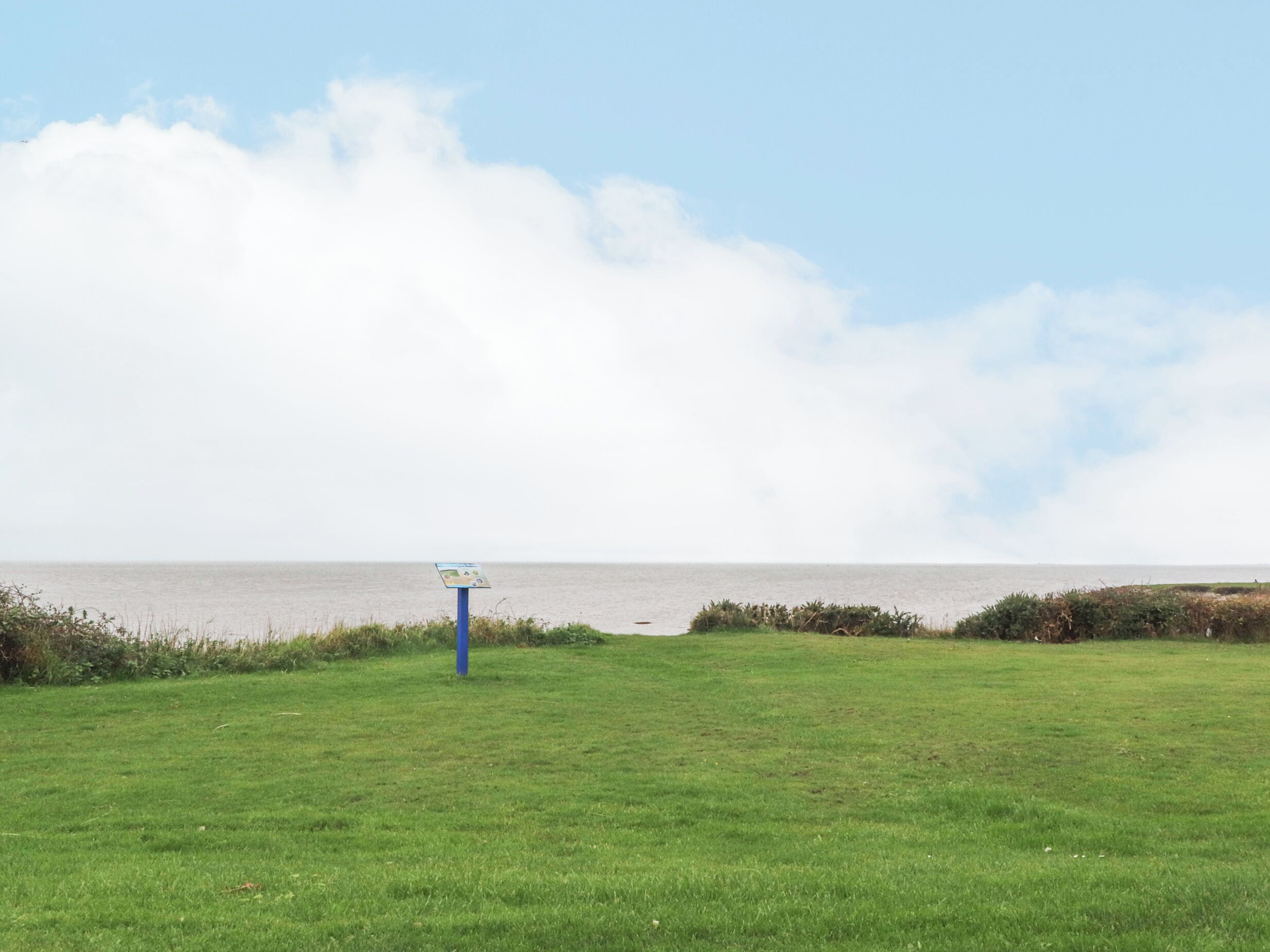 Un campo cubierto de hierba con un indicador y vista al mar.