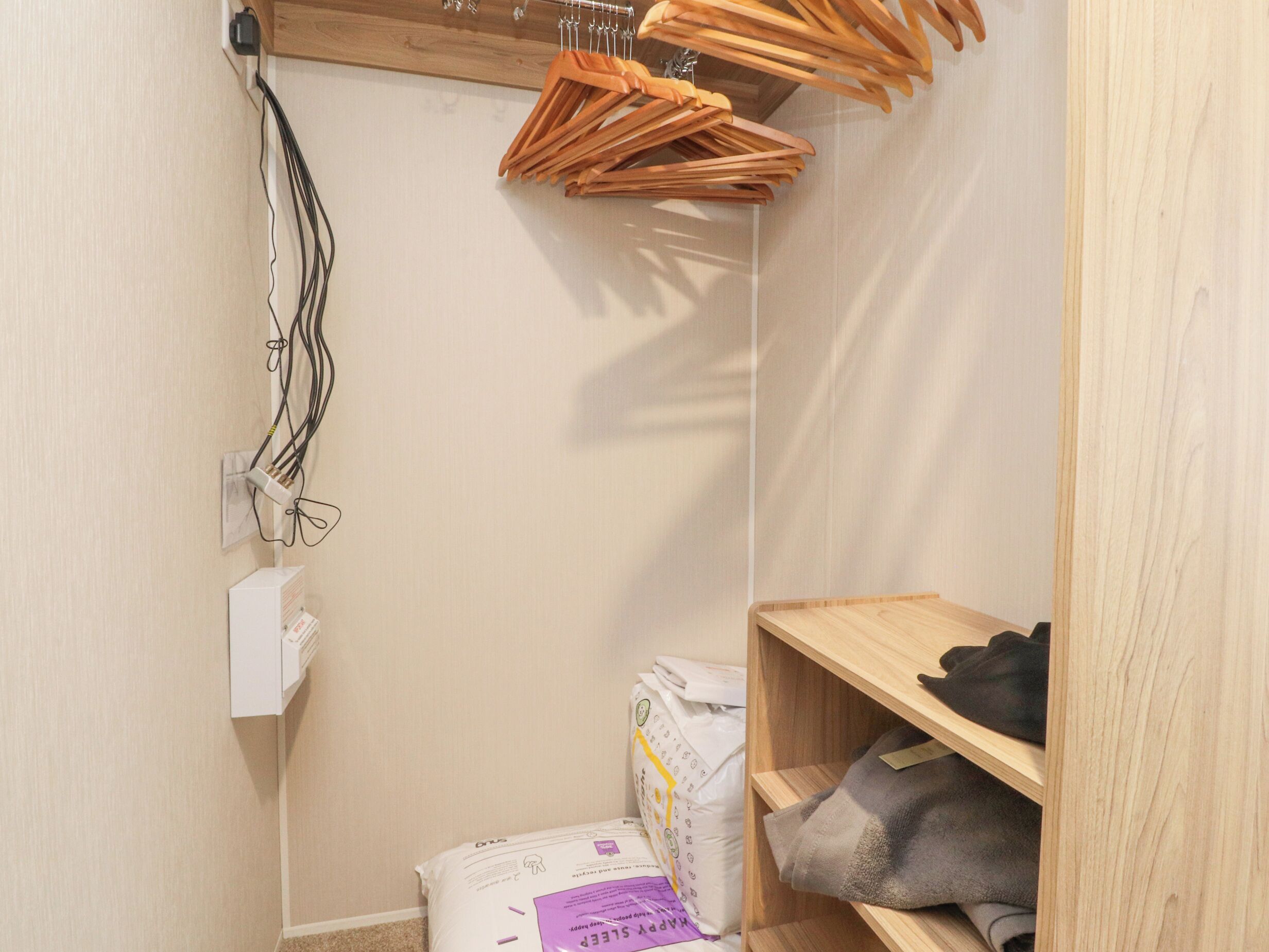 A small, narrow room with a wooden shelf, a hanging clothes rack, and a box of tissues.