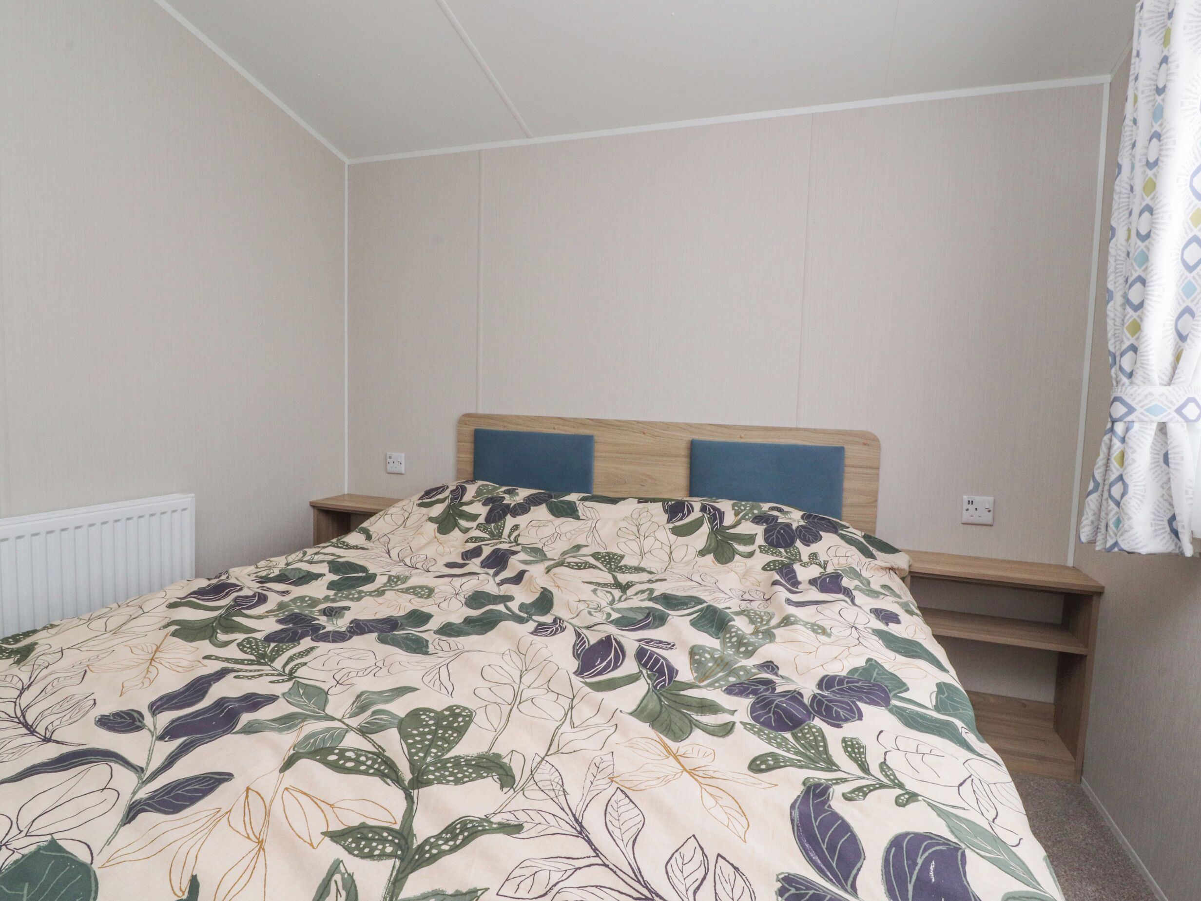 Een slaapkamer met een bed, nachtkastjes, een radiator en een raam met gordijnen.