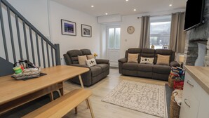 A modern living room with a sofa, a wooden dining table, and a staircase. - Bryn Tawel (Betws-Y-Coed)