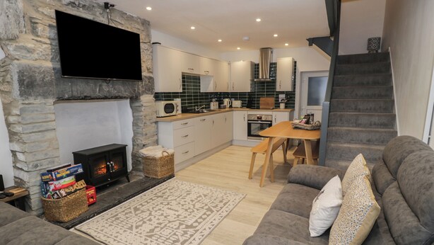 A cozy living room with a fireplace, a television mounted on a stone wall, and a grey sofa with a patterned throw. - Bryn Tawel (Betws-Y-Coed)
