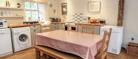Una cocina compacta con una mesa de madera, una lavadora, un microondas y una panificadora.