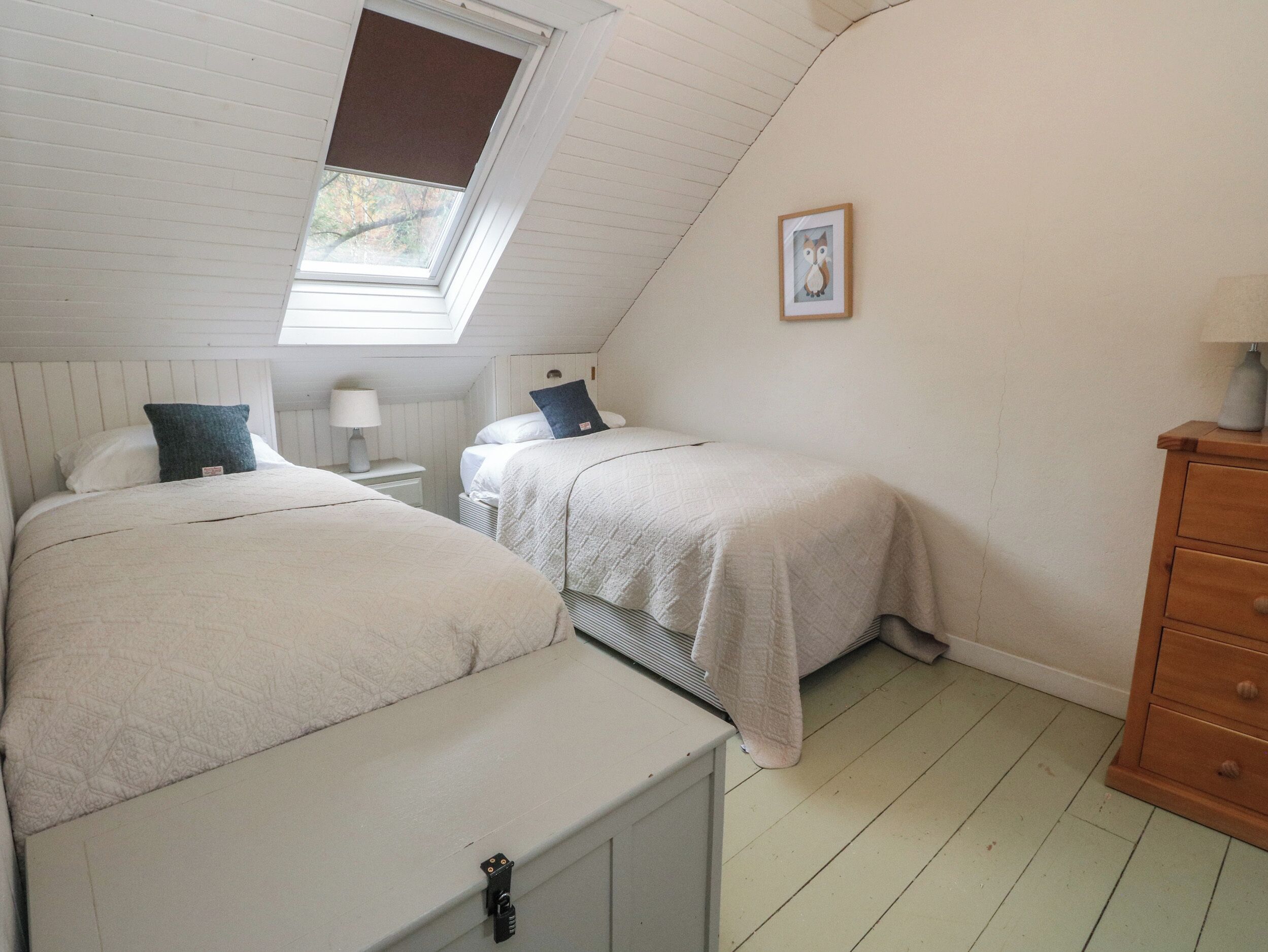 A bedroom with two beds, a window, a nightstand, a dresser, and a framed picture on the wall.
