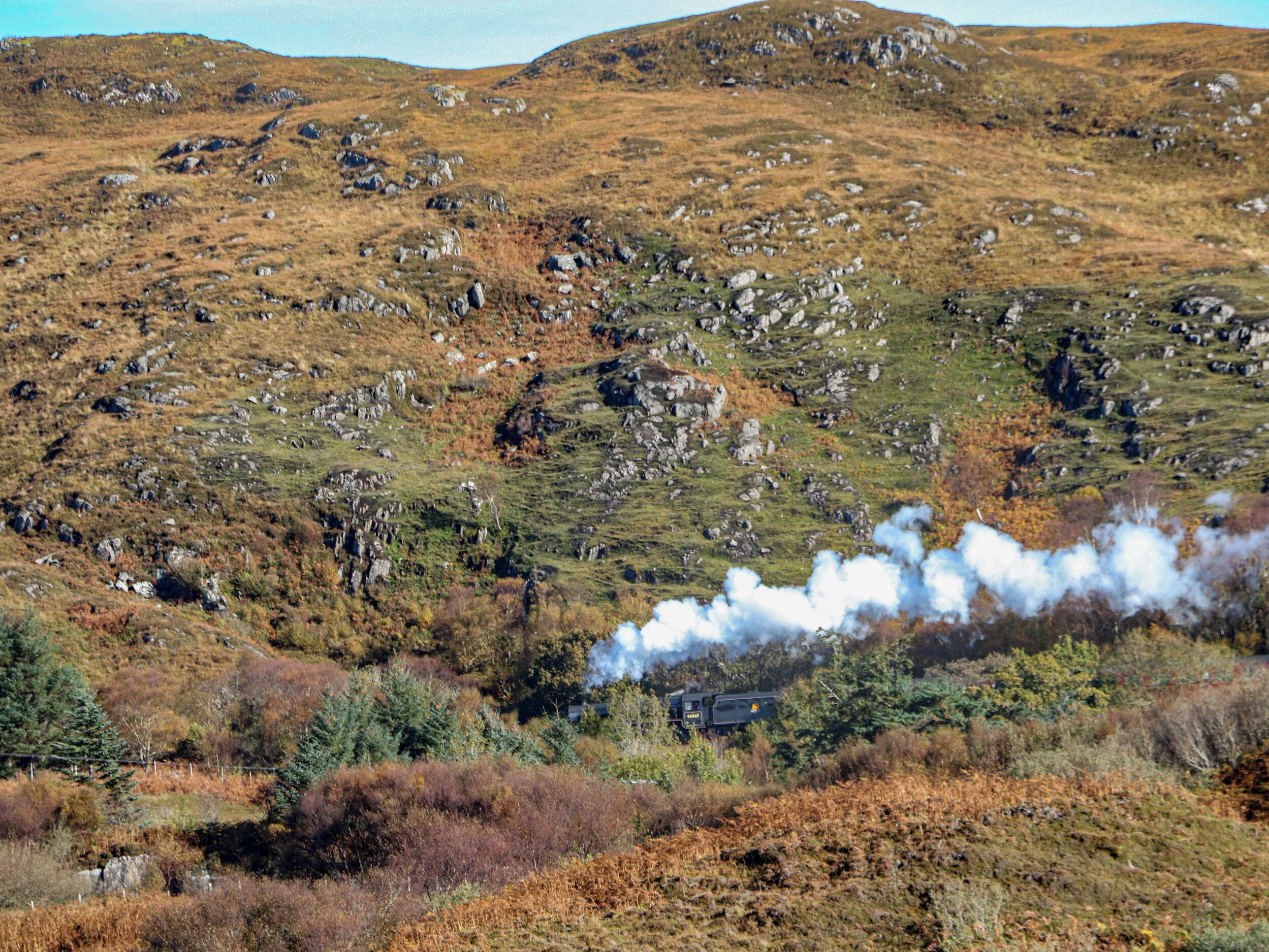 A mountainous landscape with a steam train in the foreground.