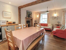 Una sala de estar acogedora con una mesa de comedor de madera, chimenea, sofá y una zona de cocina con un panera y utensilios.