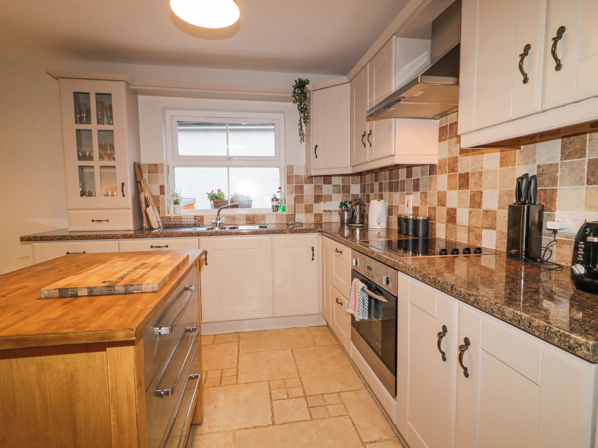 A kitchen with white cabinets, a granite countertop, a wooden cutting board, a stainless steel sink, a coffee maker, and a stove.