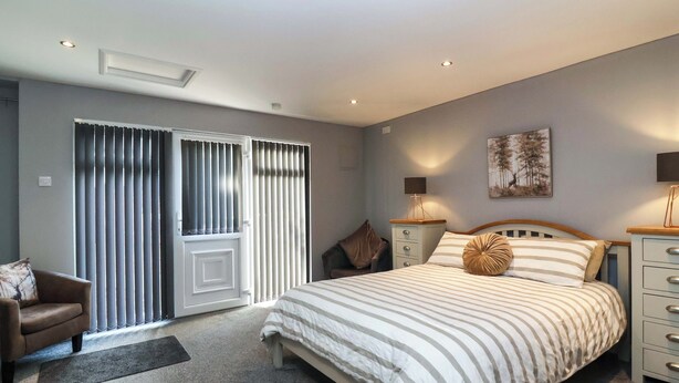 A bedroom with a bed, a nightstand, a lamp, a chair, and a sliding door. - Studio Apartment (Minehead)