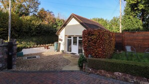 A small house with a tiled roof, a front door, and a small garden area with a gravel path leading to the entrance. - Studio Apartment (Minehead)