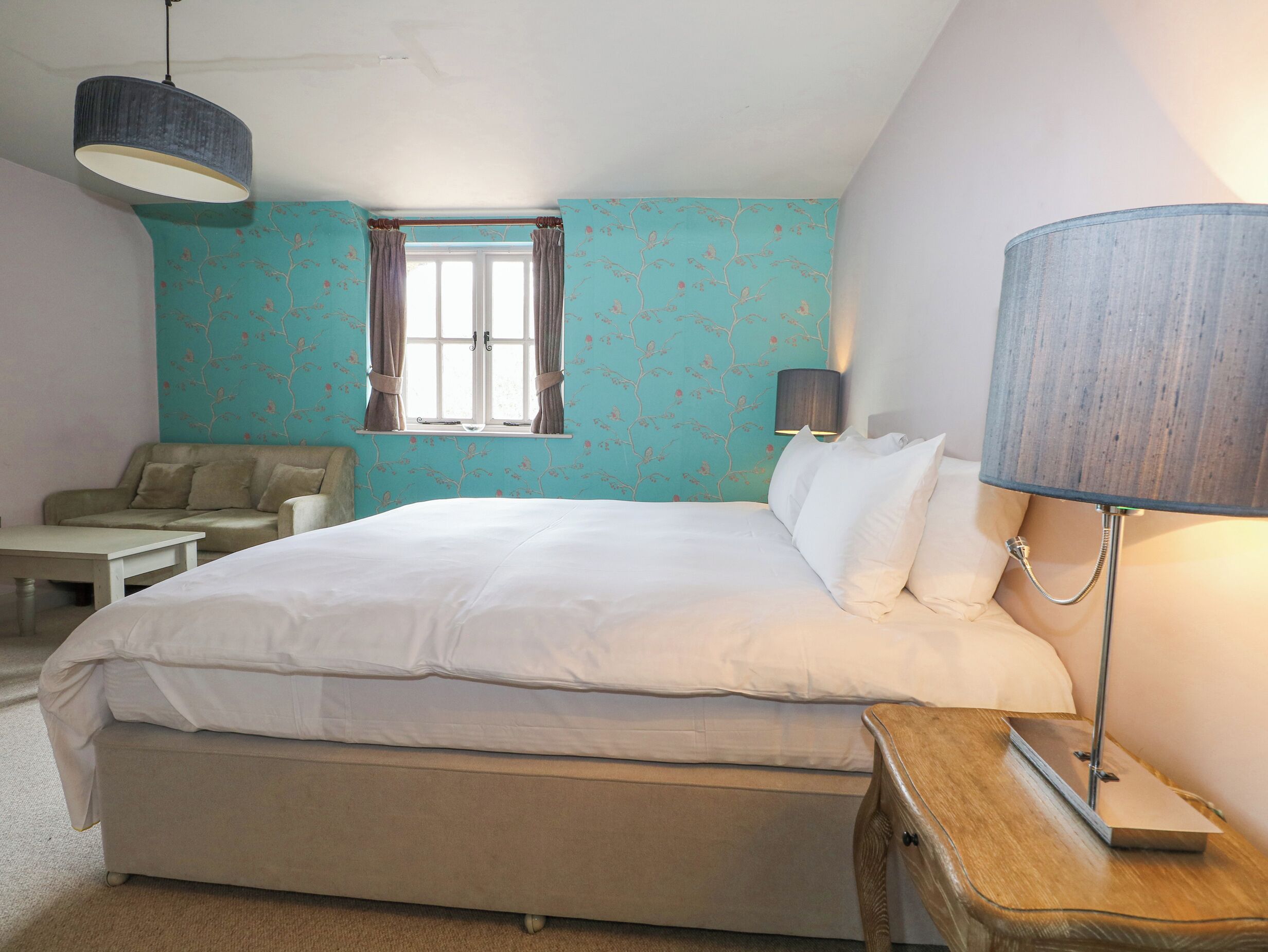 Een slaapkamer met een bed, een nachtkastje, een lamp, een raam met gordijnen en een bank.