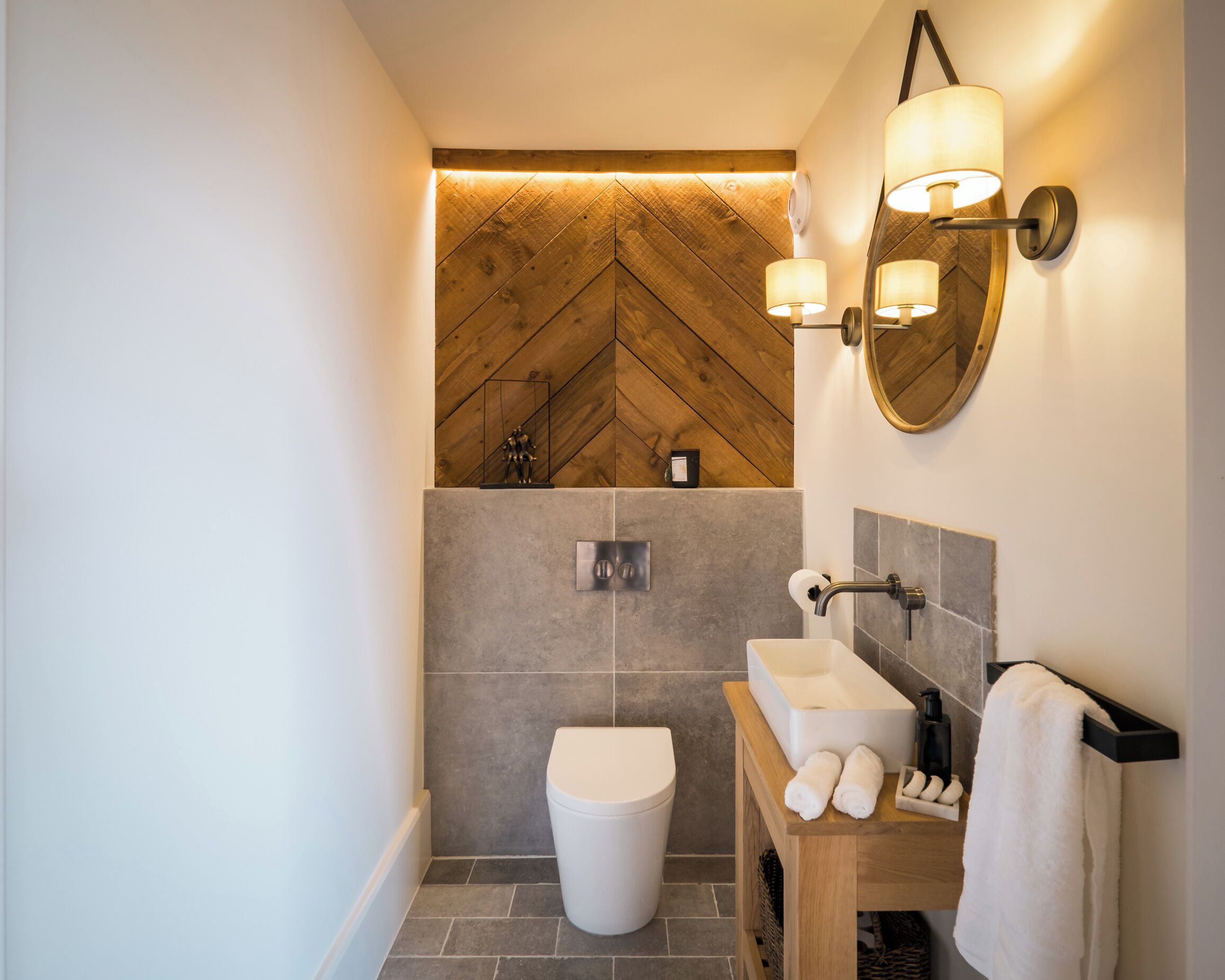 Et moderne badeværelse med loft i træ med fiskebensmønster, et hvidt toilet, en vask med spejl og en håndklæderække.
