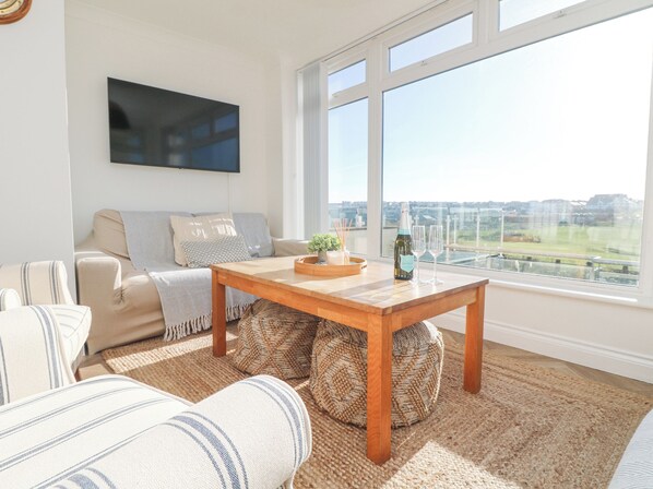 A living room with a sofa, a wooden coffee table, and a large window with a city view. - 5 Fistral Waves (Newquay)