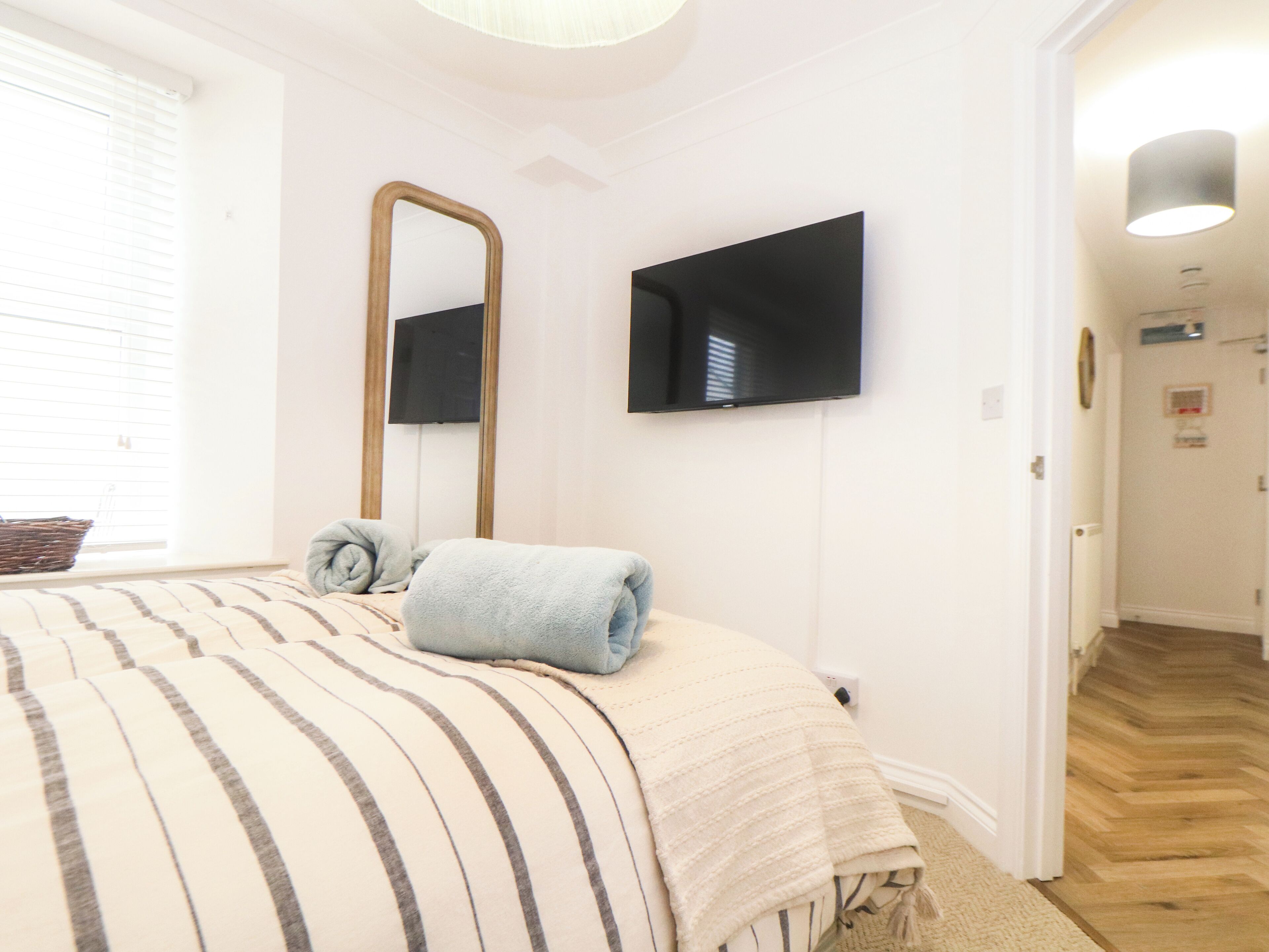 A bedroom with a bed, a large mirror, a flat-screen TV, and a window with blinds.
