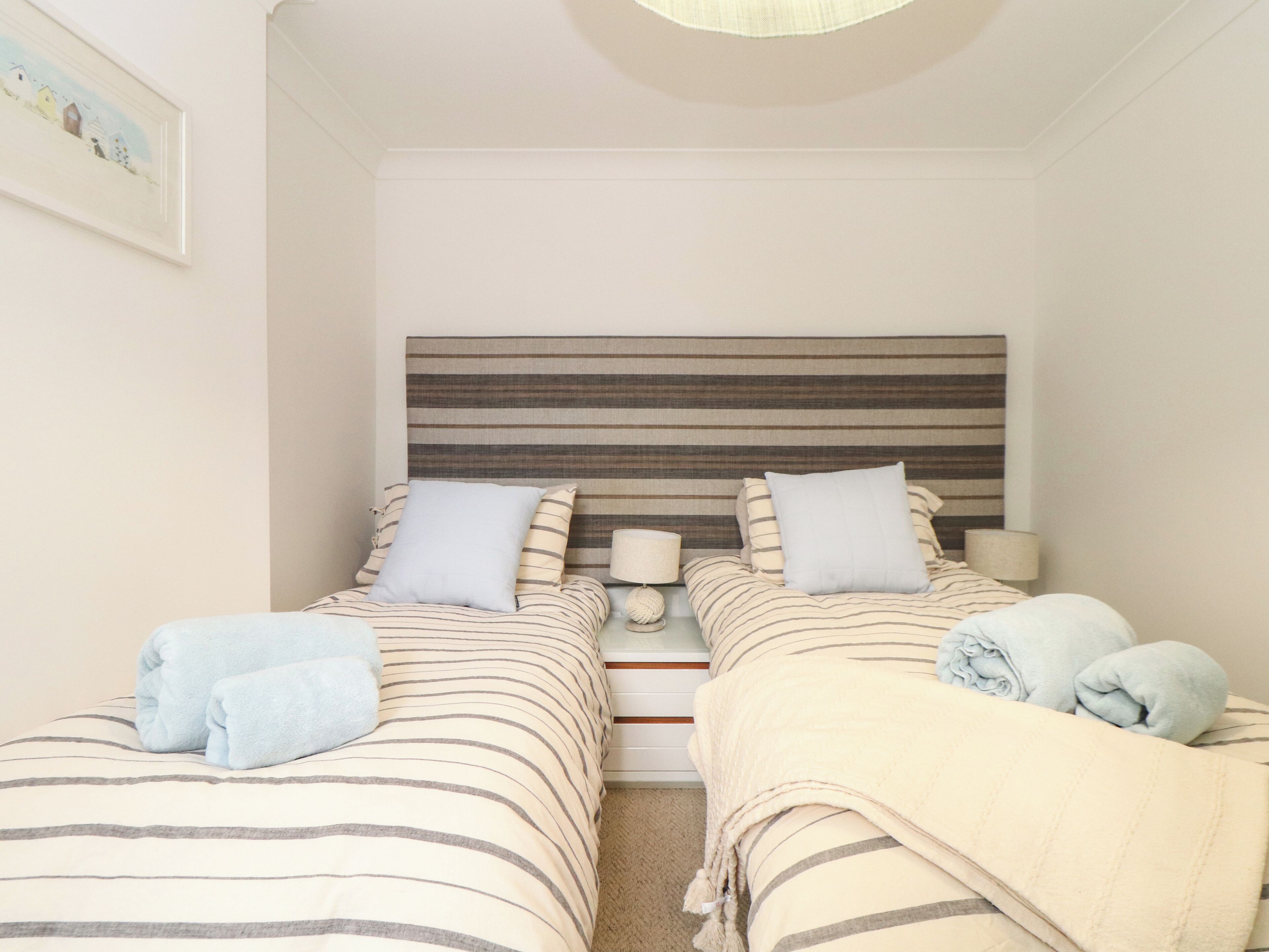 A twin room with two beds, each with striped bedding and pillows, a bedside table with a lamp, and a headboard with horizontal stripes.