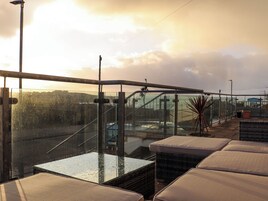 A rooftop terrace with glass railings, cushioned seating, and a view of the cityscape.