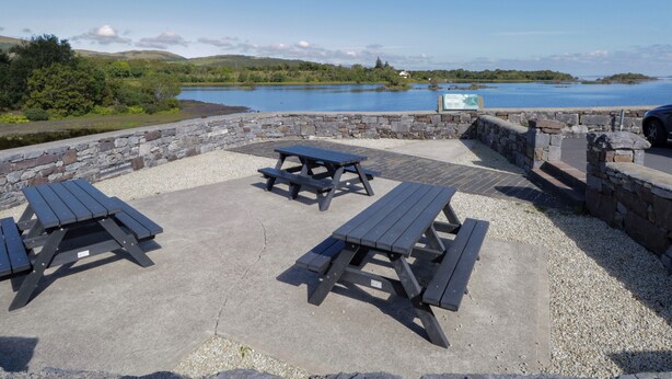 A picnic area with stone walls and benches overlooking a lake. - Robins Roost 2 (Cornamona)