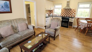 A living room with a sofa, armchairs, and a coffee table. There is a kitchen area with a stove, sink, and cabinets. - Robins Roost 2 (Cornamona)