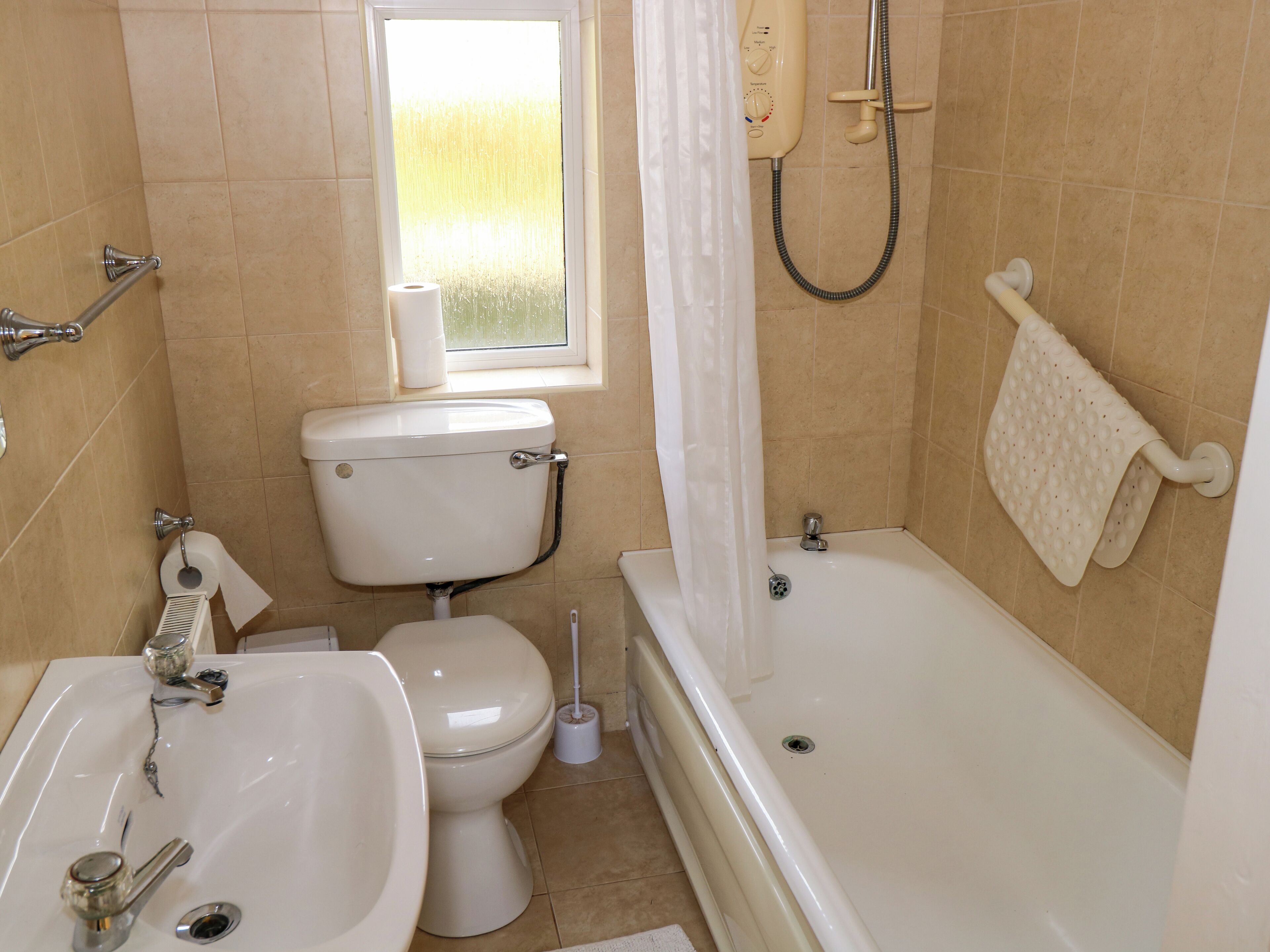 A bathroom with a toilet, sink, bathtub, shower, and a window with a view.