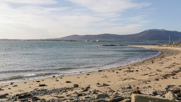 A beach with a rocky shoreline, calm sea, and distant mountains under a clear sky. - Ritas (Newry)