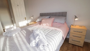 A neatly made bed with rolled towels, a bedside lamp, and a wooden nightstand with drawers. - Ritas (Newry)