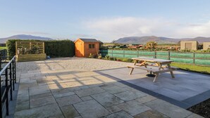 A patio area with a wooden shed, a picnic table, and a view of a green field and mountains in the distance. - Ritas (Newry)