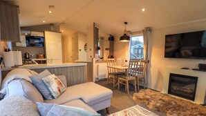 A cozy living room with a sofa, a fireplace, and a television. - Highlands Way Lodge (Workington)