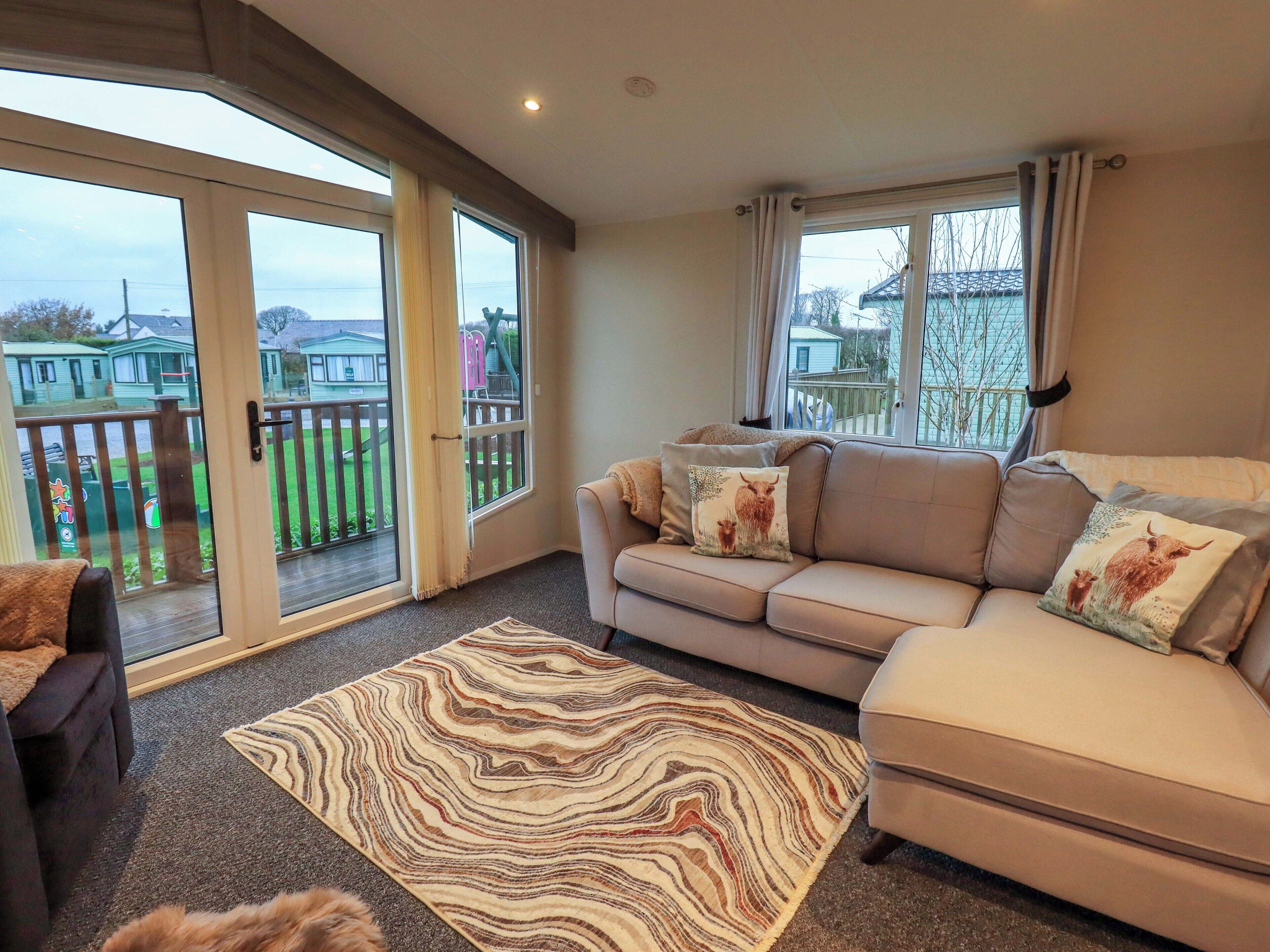 A living room with a beige sofa, patterned rug, and large windows with curtains.