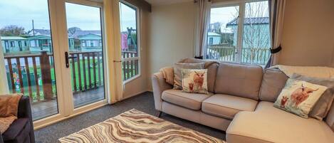 A living room with a beige sofa, patterned rug, and large windows with curtains.