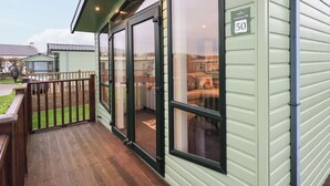 A caravan numbered 50 with a wooden deck and a glass door leading to a furnished interior. - Highlands Way Lodge (Workington)