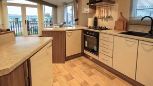 A modern kitchen with a built-in oven, a gas stove, and a sink. There is a balcony with a view of the outside. - Highlands Way Lodge (Workington)