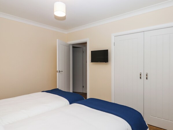 A bedroom with two beds, a TV on the wall, and a wardrobe.