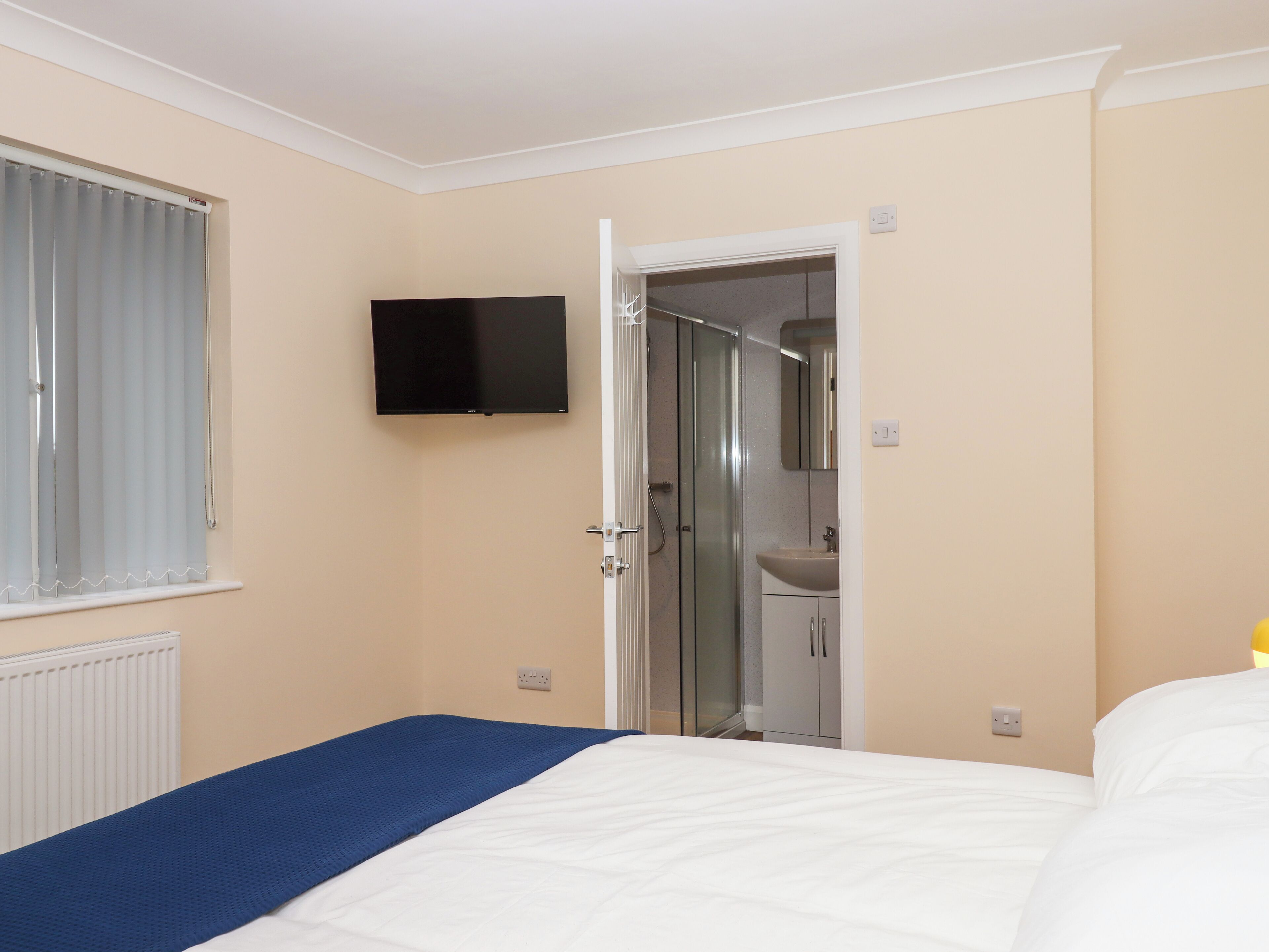 Una habitación de hotel con cama, televisión montada en la pared, zona de ducha y baño con lavamanos.
