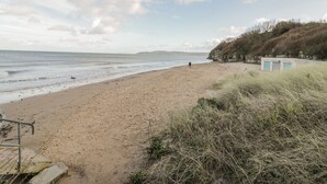 A beach with a sandy shore, a person walking, and a small building on the right. - Seaview (Tyn-y-Gongl)