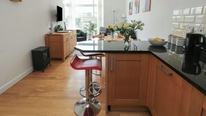 A modern kitchen with wooden cabinets, a black countertop, and a bar stool. - Seaview (Tyn-y-Gongl)