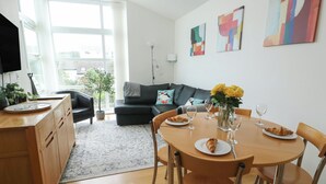 A modern living room with a dining area, featuring a sofa, a coffee table, and a dining table set for two. - Seaview (Tyn-y-Gongl)