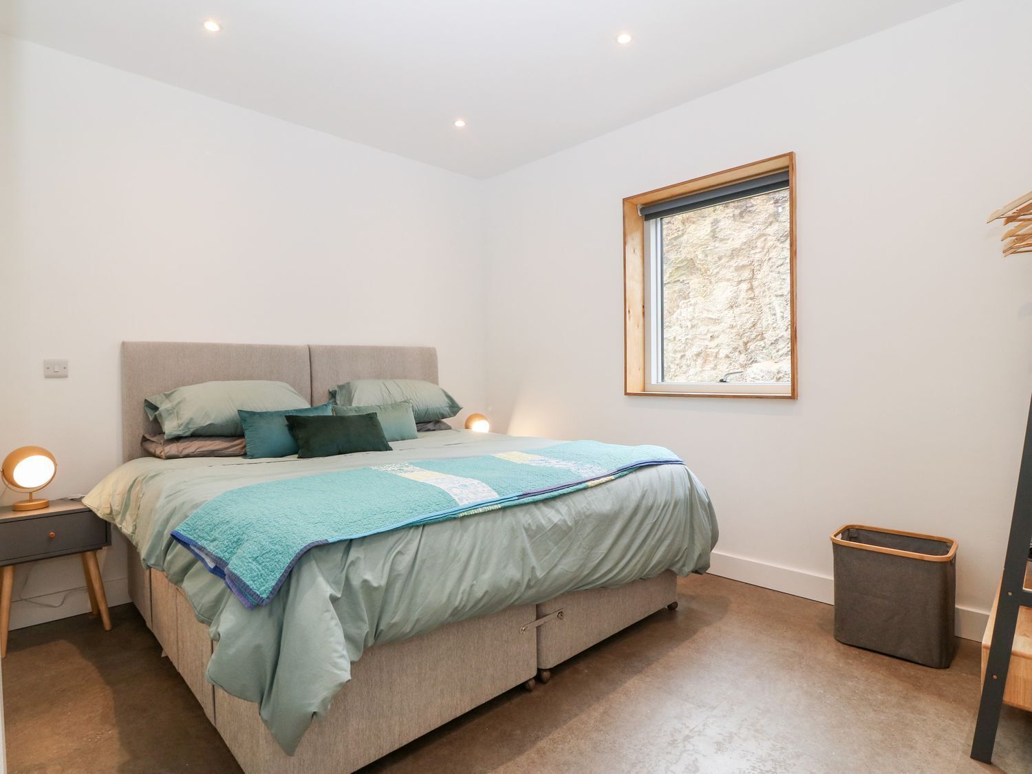 A bedroom with a bed, bedside tables, a window, and a trash bin.