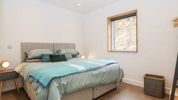 A bedroom with a bed, bedside tables, a window, and a trash bin.