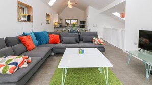 A modern living room with a sectional sofa, a white coffee table, and a TV on a glass table. - Ty Chwarel (Bangor)