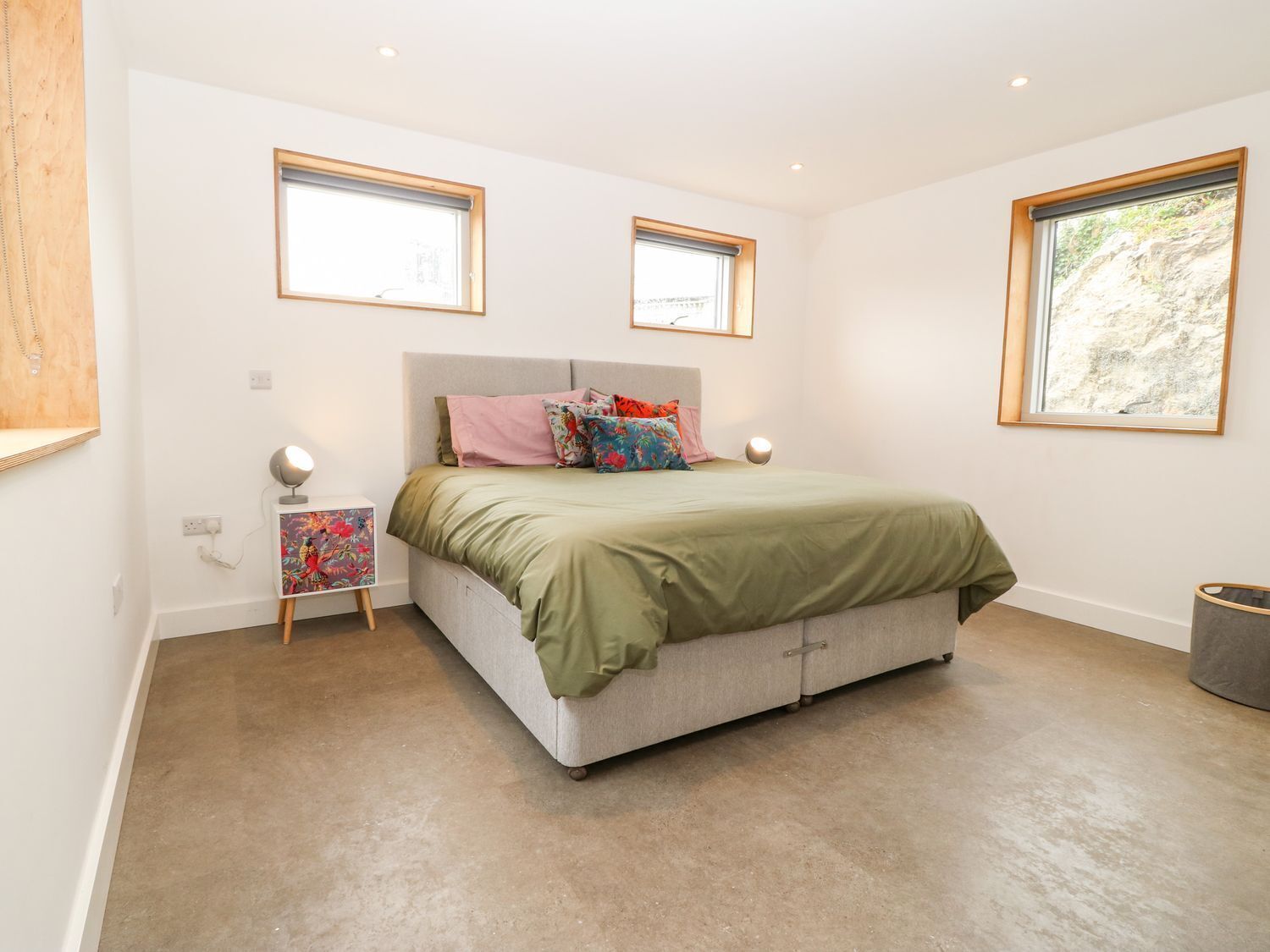A bedroom with a bed, two windows, a bedside table, and a lamp.