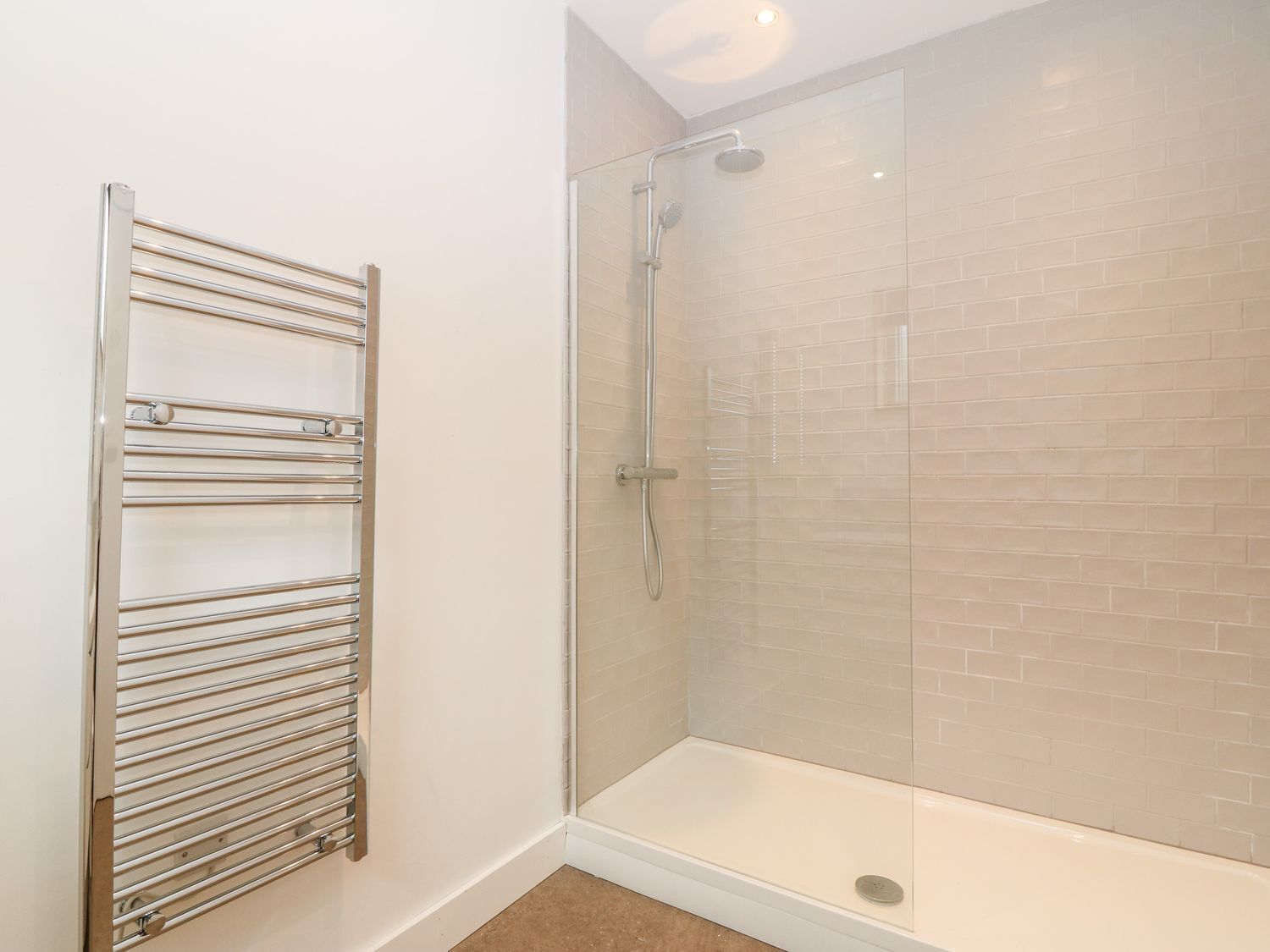 A glass-enclosed shower with a white tiled wall and a chrome towel rack.