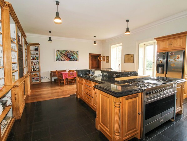 A spacious kitchen with wooden cabinets, a central island, and a stainless steel refrigerator. - Caynham Court (Ludlow)