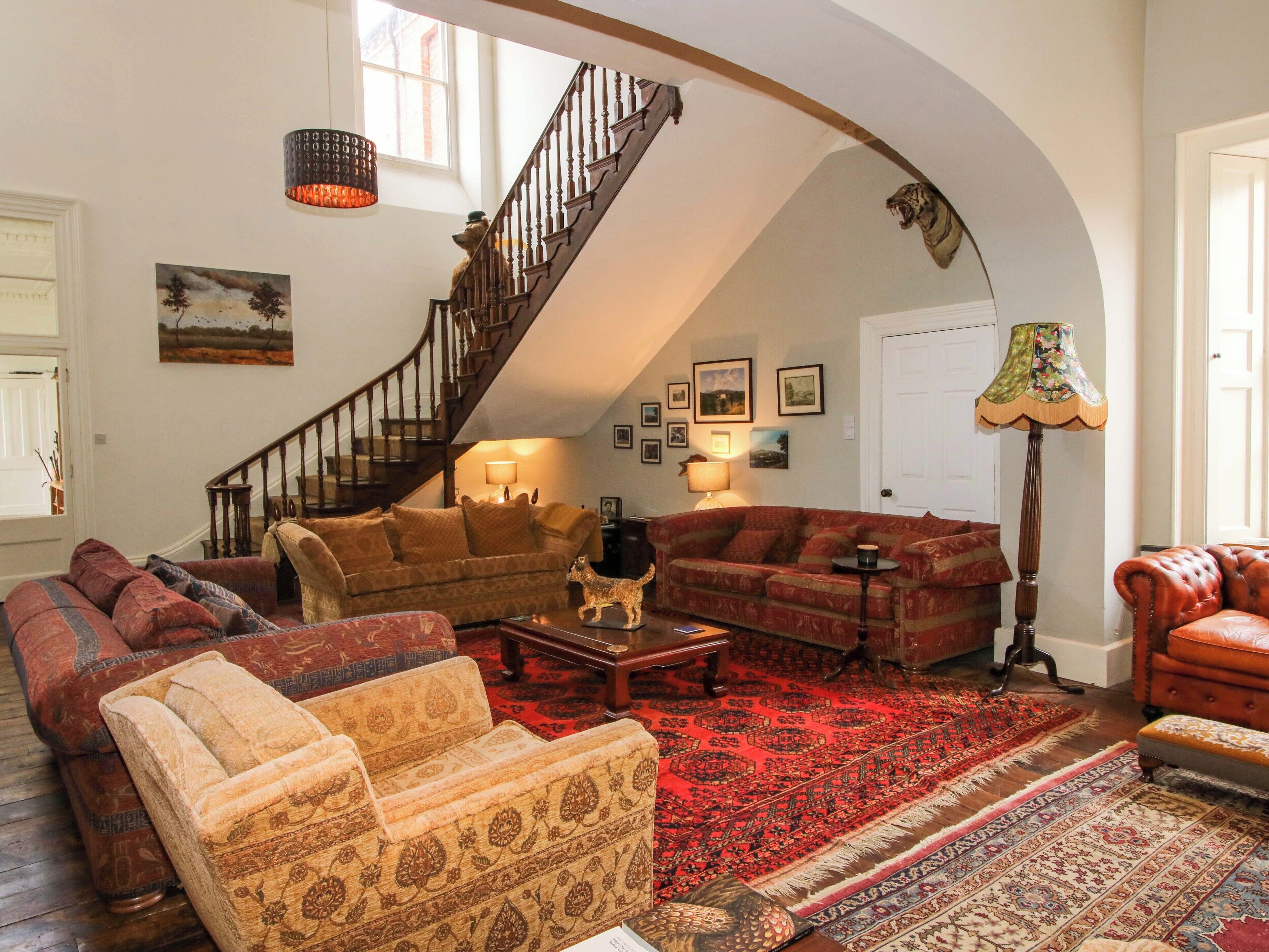 A spacious living room with a high arched ceiling, a wooden staircase, and multiple seating areas.