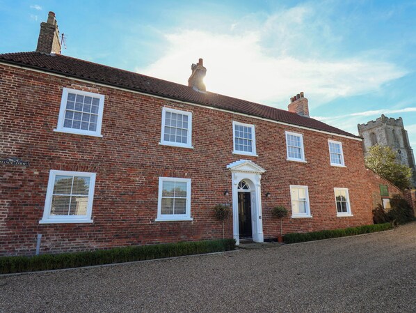 A red brick building with a symmetrical facade, a central entrance with a white door, and a small garden area in front. - Harpham Manor House (Driffield)