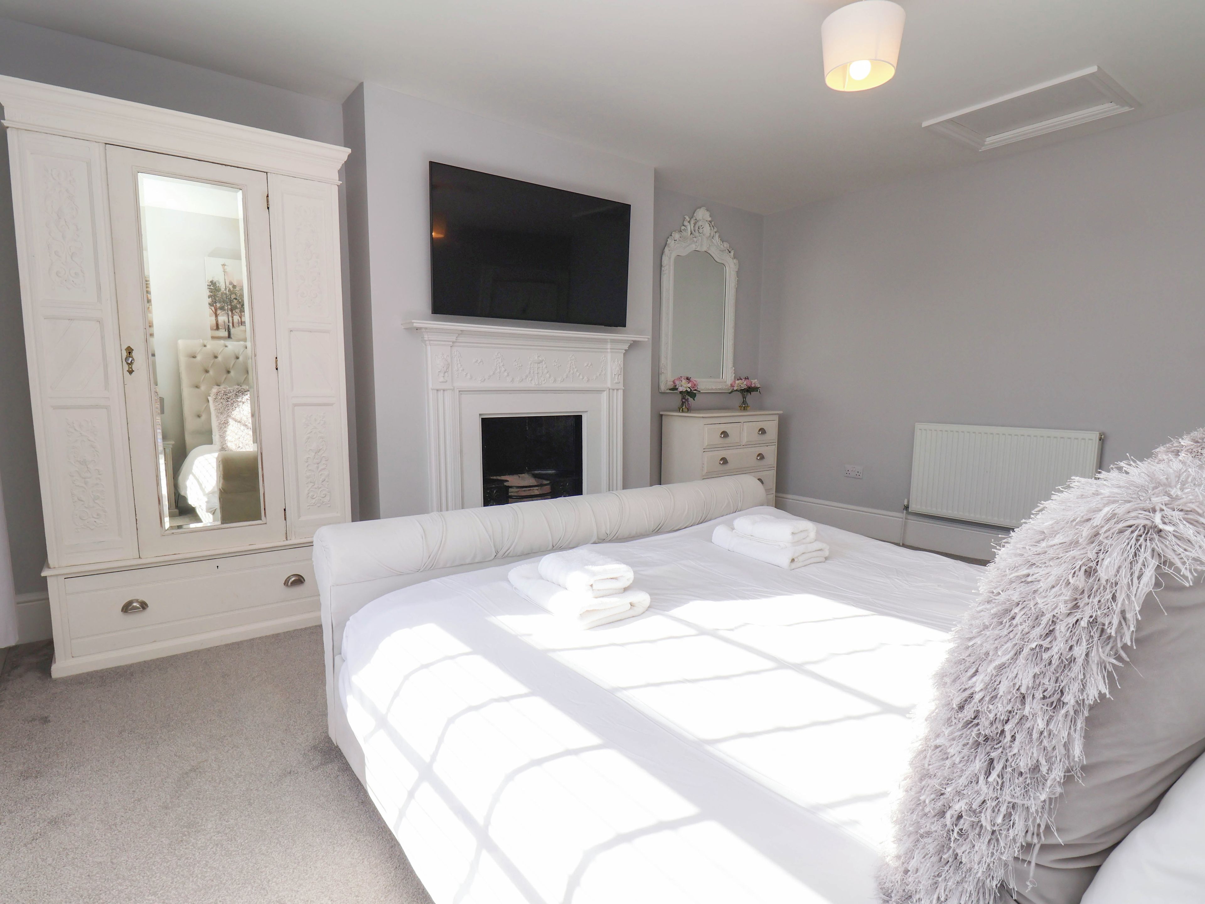 Een slaapkamer met een bed, een dressoir, een televisie, een open haard en een spiegel.